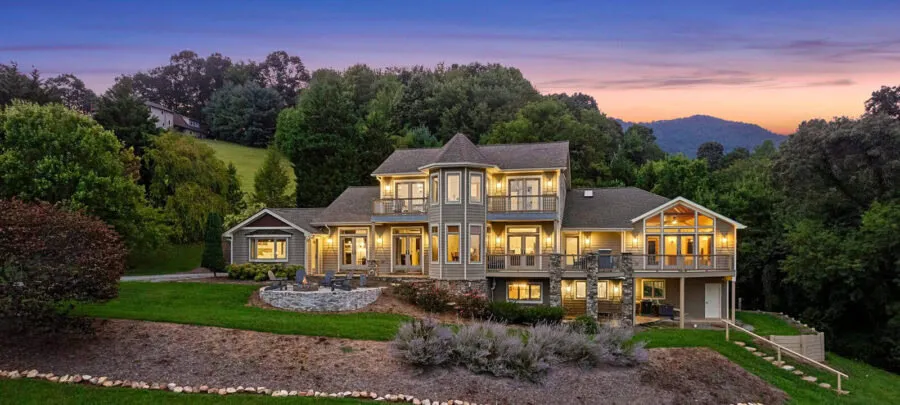 Elegant multi‑story house on a landscaped hillside at dusk with glowing interior lights